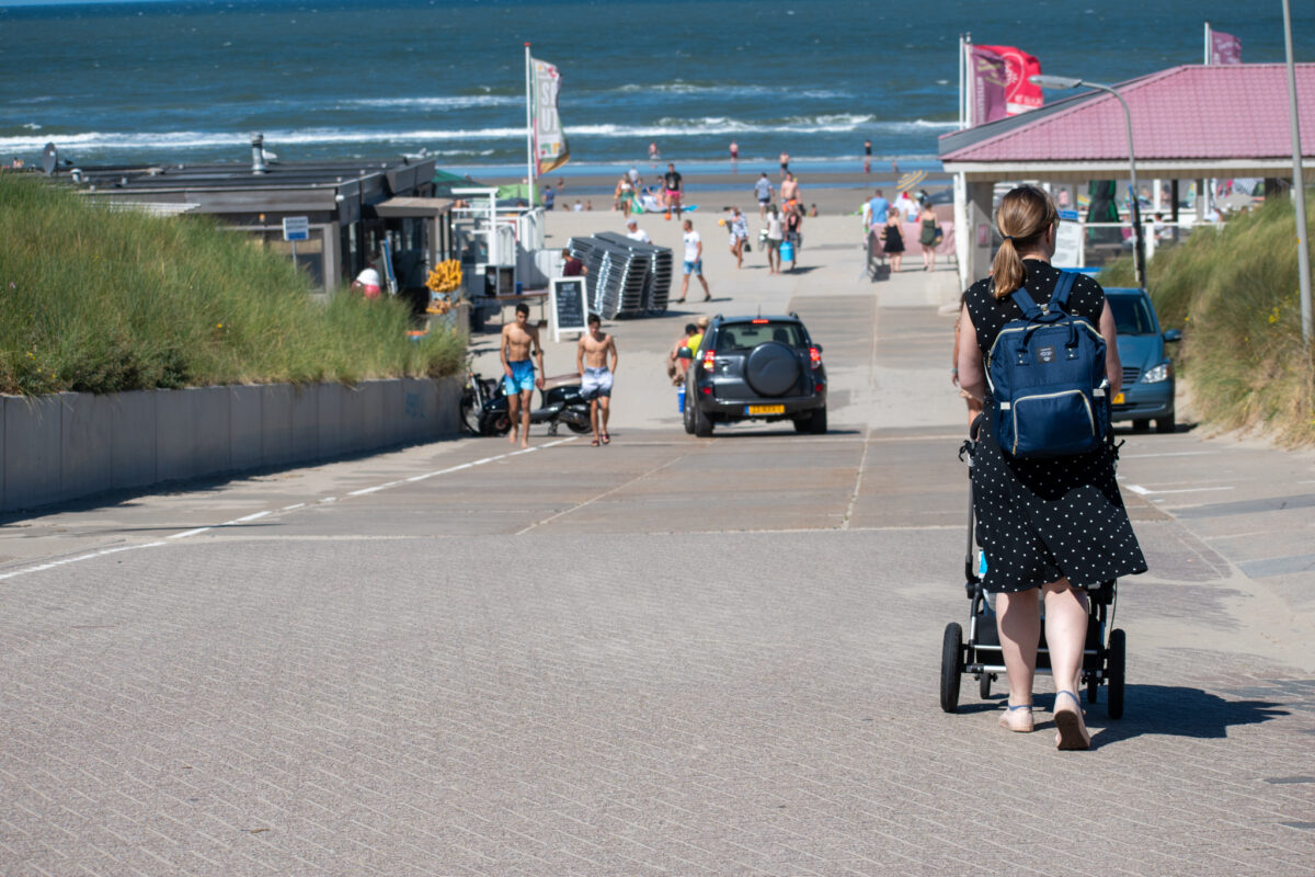 Vrouw op het strand met kinderwagen en luiertas
